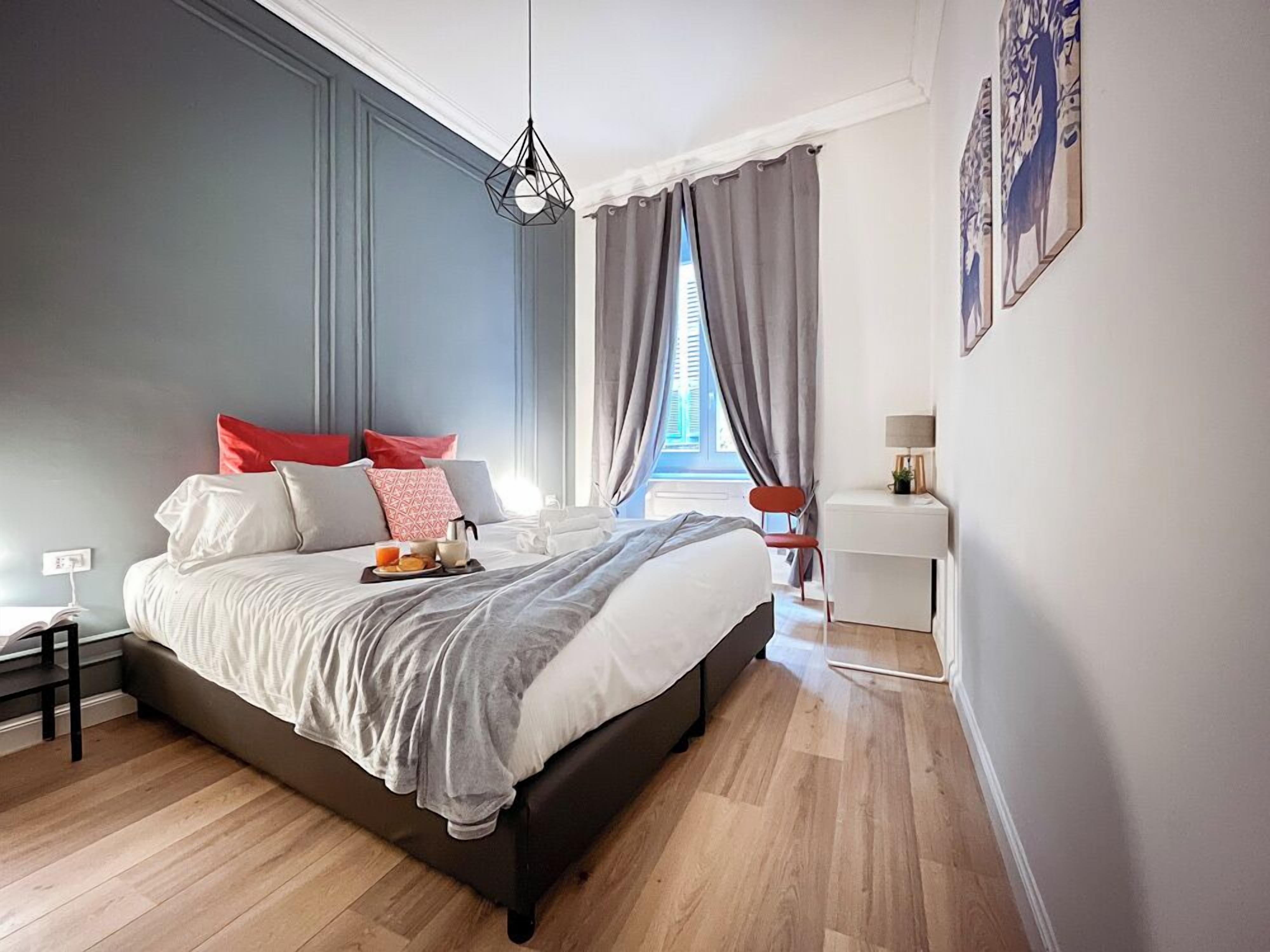 A modern bedroom with a large bed, a bedside table, a desk, and a window with curtains.