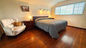 A bedroom with a bed, a chair, a nightstand, a lamp, a picture on the wall, and a window. - Delightful Spacious 3-bedroom Home in Silicon Valley (Santa Clara)