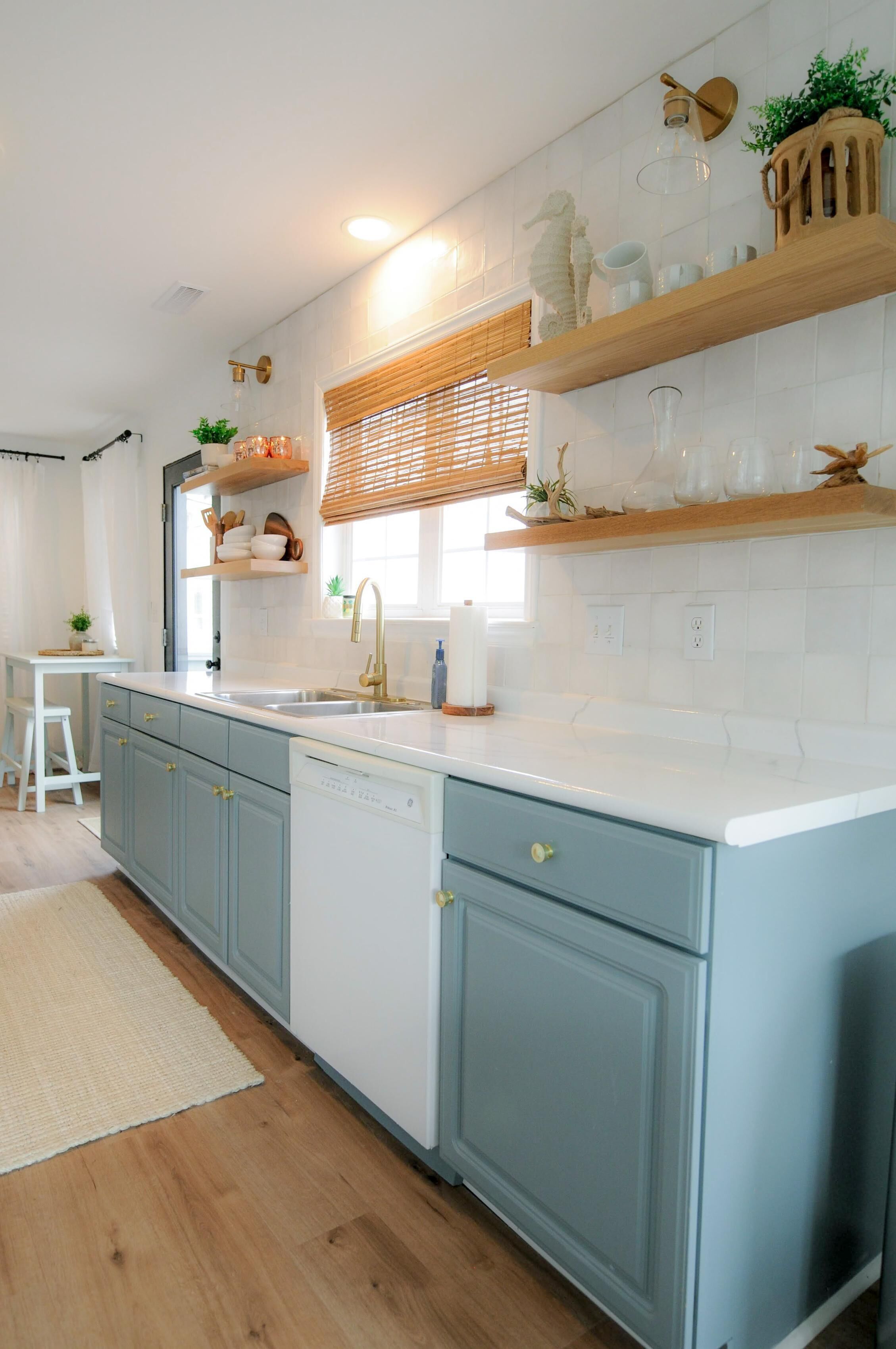 A kitchen with light blue cabinets, a white countertop, and wooden shelves above.