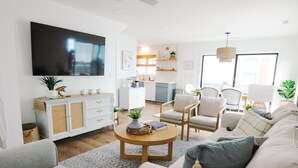 Un salon moderne avec un téléviseur à écran plat, une table basse ronde et un canapé. Il y a également un coin cuisine avec une table à manger et des chaises.