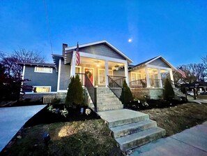 A two-story residential building with a front porch, a flag, and a well-maintained lawn.