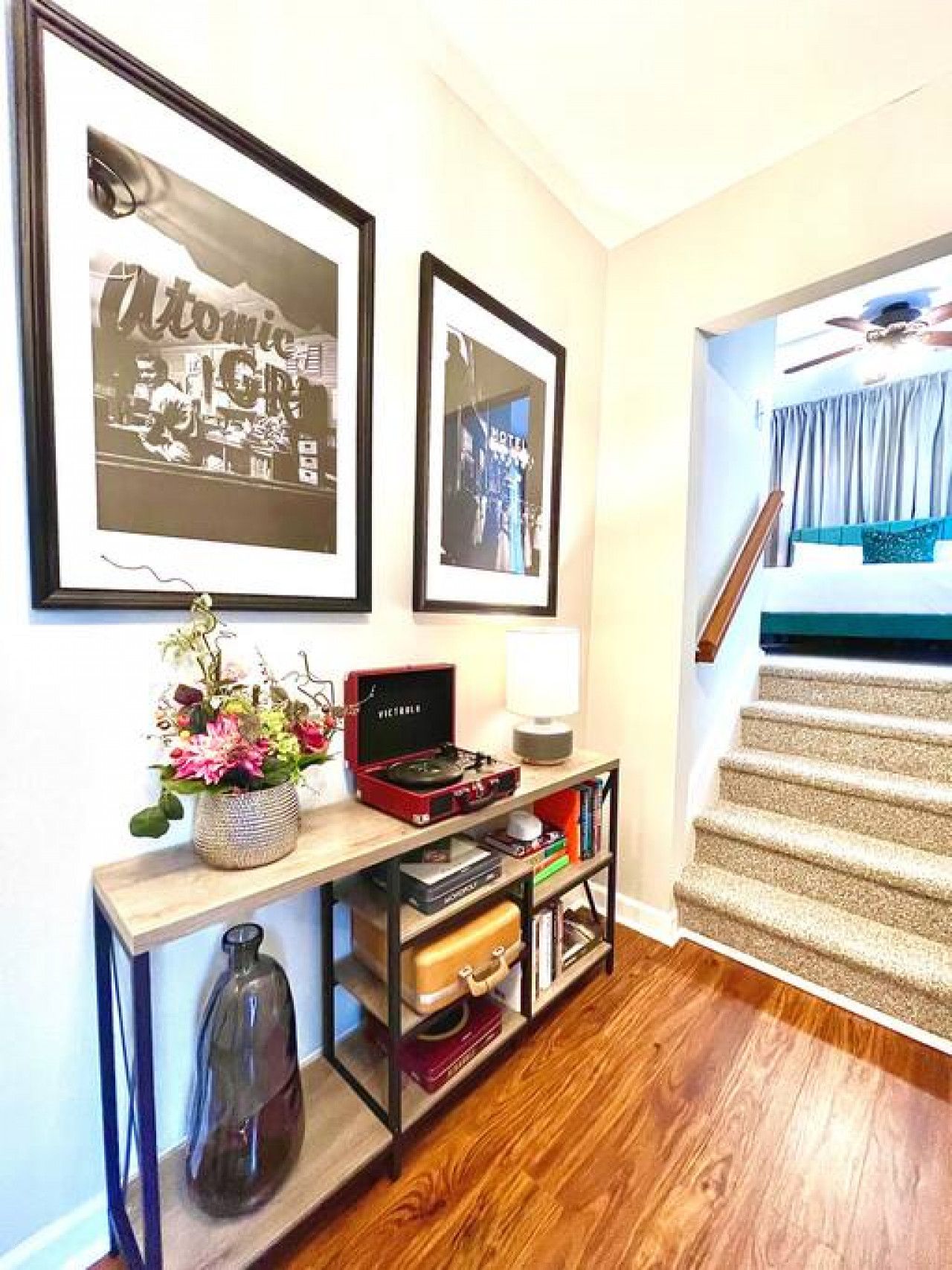 Un couloir avec un escalier, une console sur laquelle est posé un tourne-disque, et deux tableaux encadrés accrochés au mur.