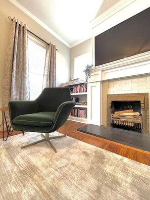 A living room with a green armchair, a fireplace, a bookshelf, and a large flat-screen TV.