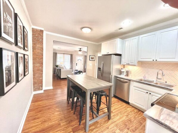 A kitchen with a wooden table, bar stools, a refrigerator, and white cabinets.
