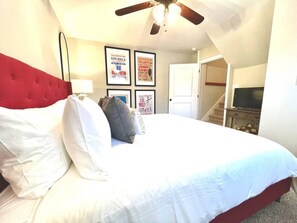 A bedroom with a bed, a ceiling fan, a television, and framed posters on the wall.