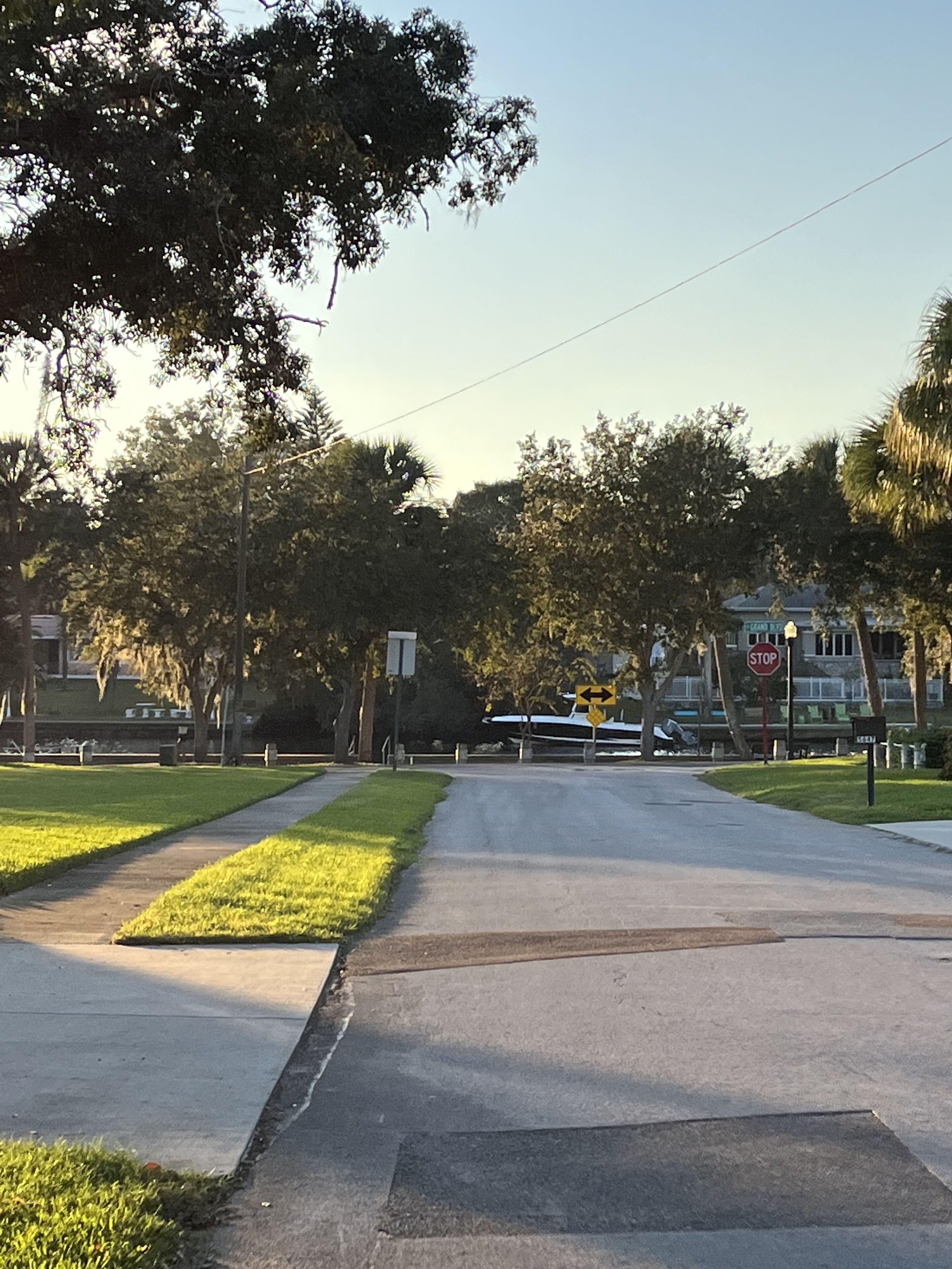 A quiet suburban street with a sidewalk, grassy areas, and trees.