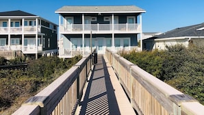 Una propiedad frente a la playa con un paseo marítimo de madera que conduce a un edificio de dos pisos con balcones.