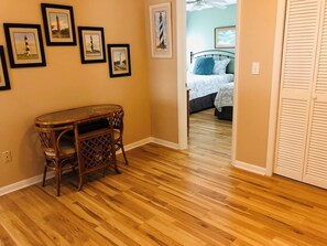 A hallway with wooden flooring, a wicker table, and a bed with a blue pillow.