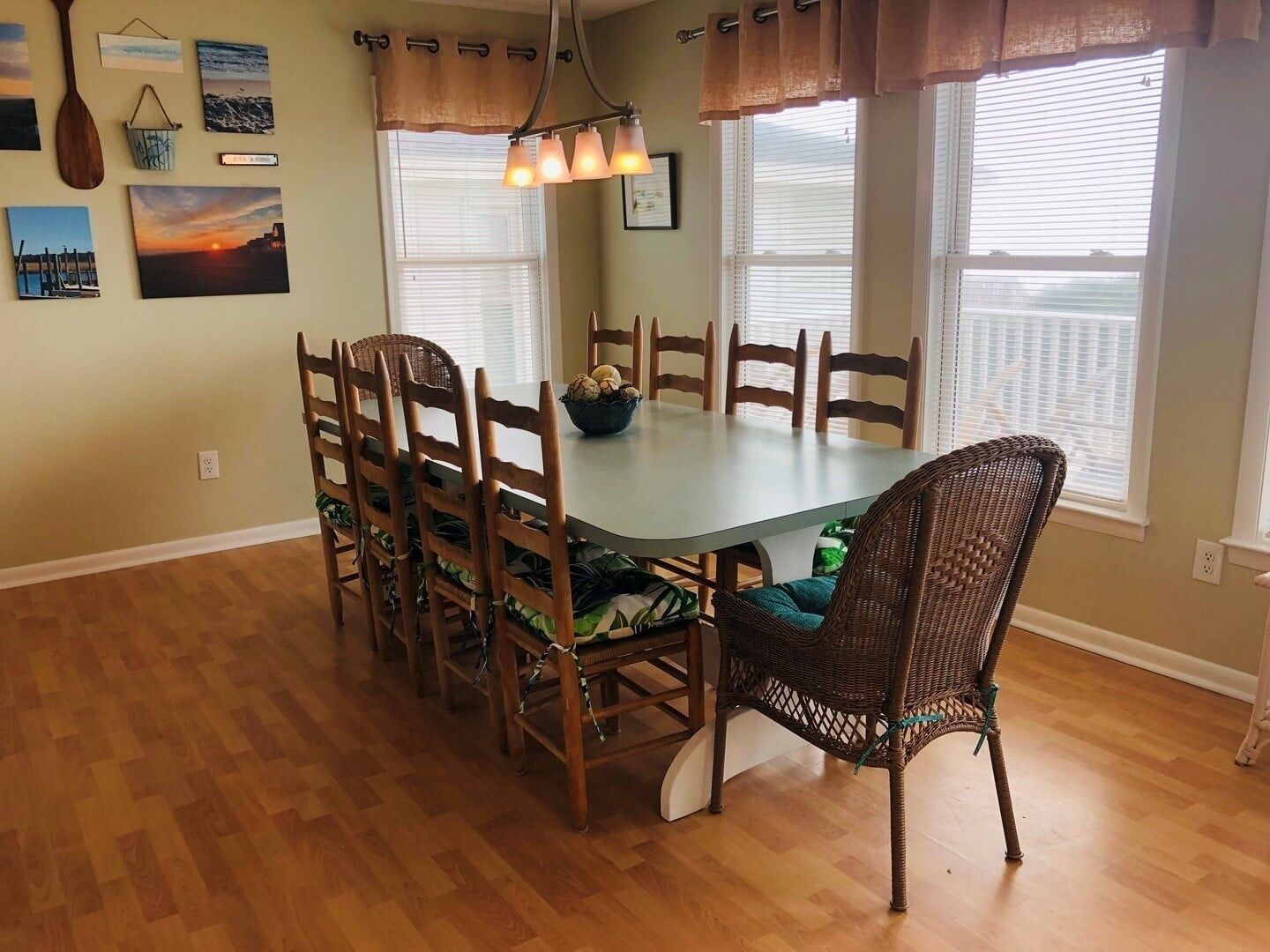 Comedor con una mesa redonda, sillas de madera, un sillón de mimbre y una pared decorada con cuadros.