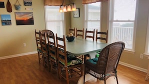 Comedor con una mesa redonda, sillas de madera, un sillón de mimbre y una pared decorada con cuadros.