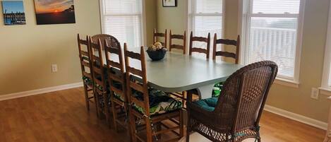 Comedor con una mesa redonda, sillas de madera, un sillón de mimbre y una pared decorada con cuadros.