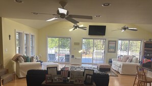 A spacious living room with a high ceiling, ceiling fans, a large window, and a sliding glass door leading to a patio.
