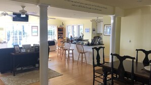 A spacious living area with a dining table and chairs, a kitchen in the background, and a motivational quote on the wall.