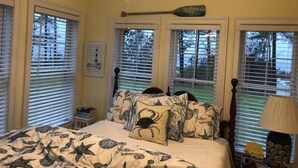 A bedroom with a bed, a ceiling fan, and windows with blinds.