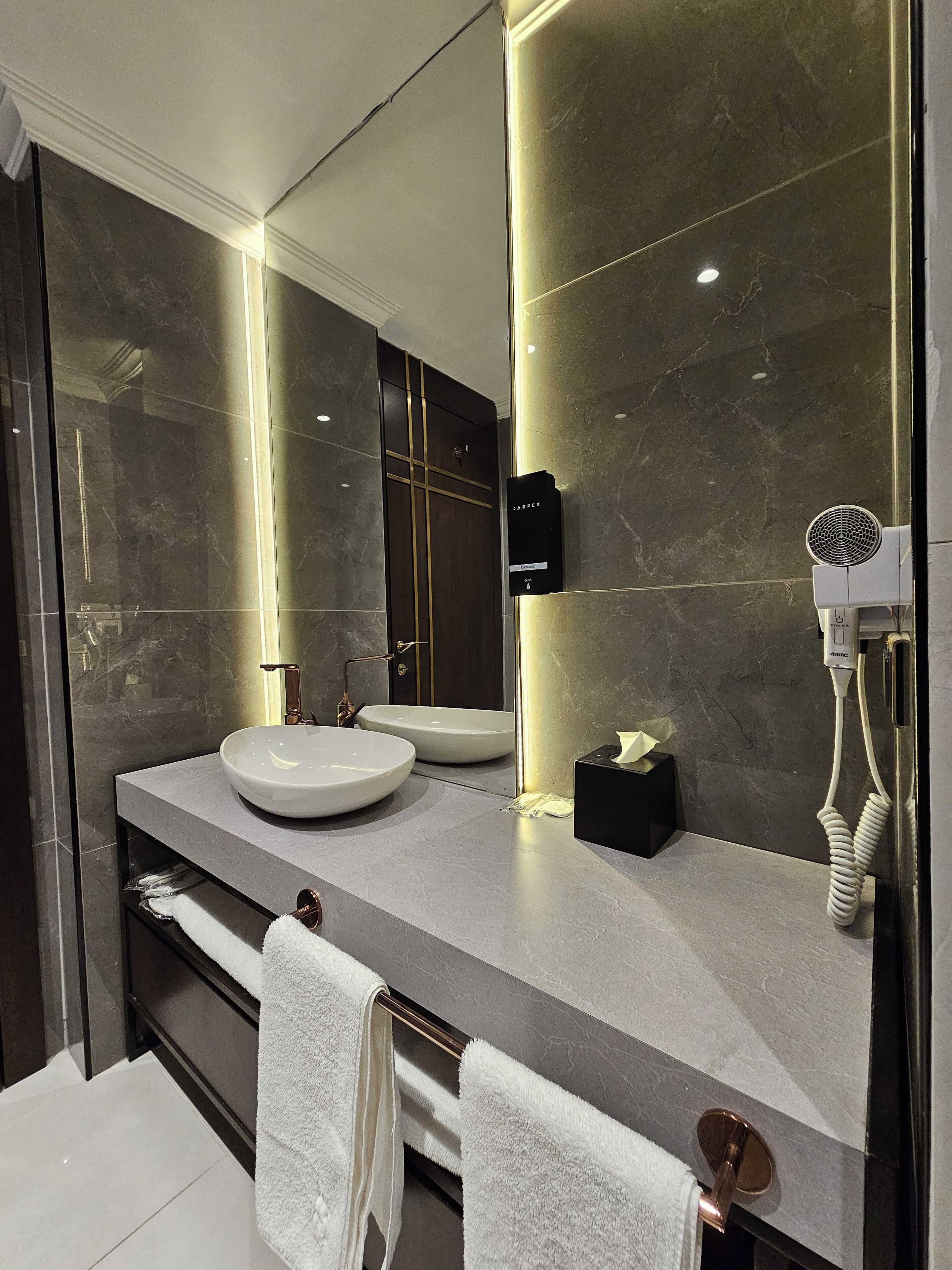 A modern bathroom with a large mirror, two sinks, and a towel rack.