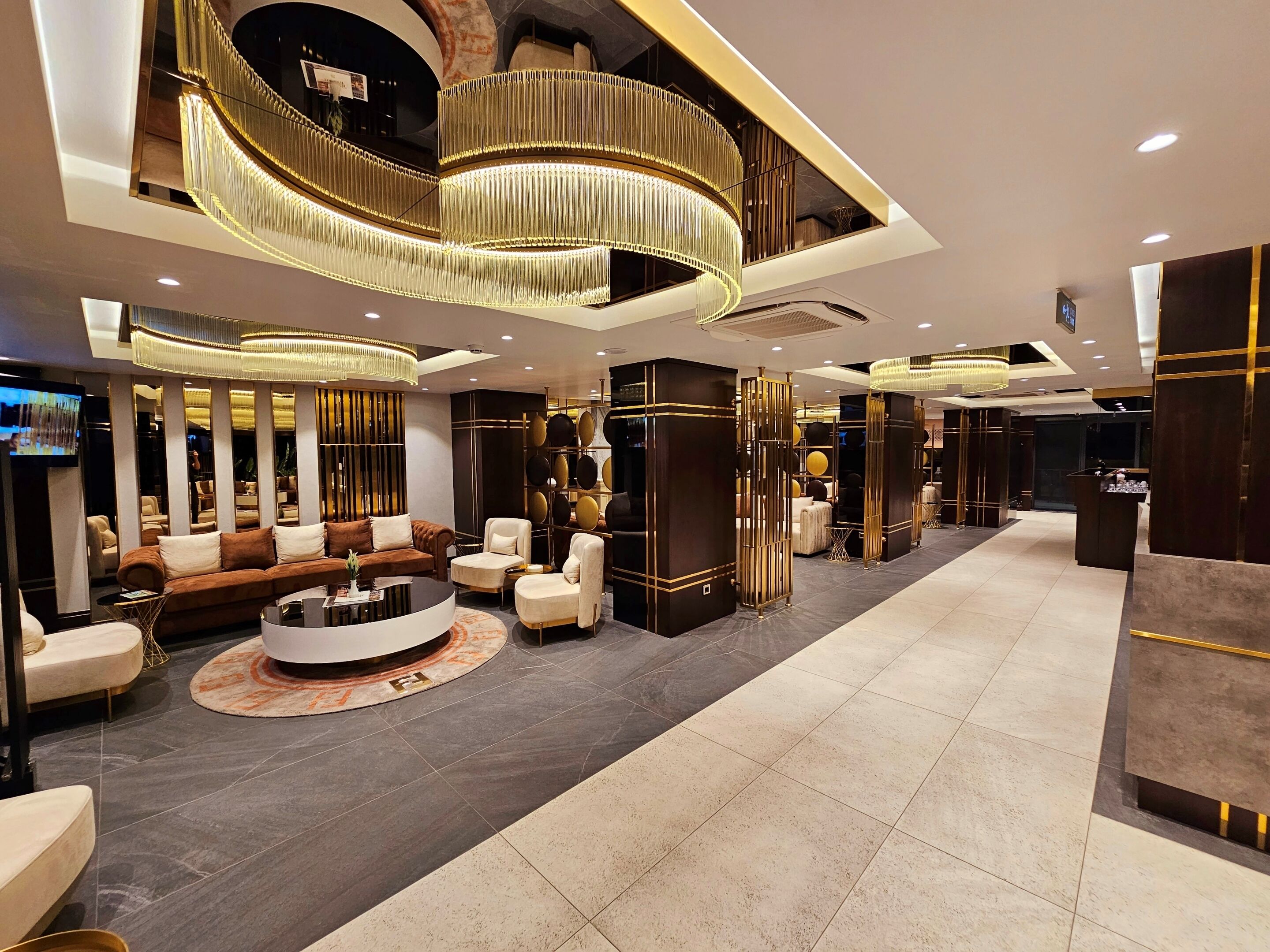 A modern lobby with a central seating area, a reception desk, and a large chandelier.