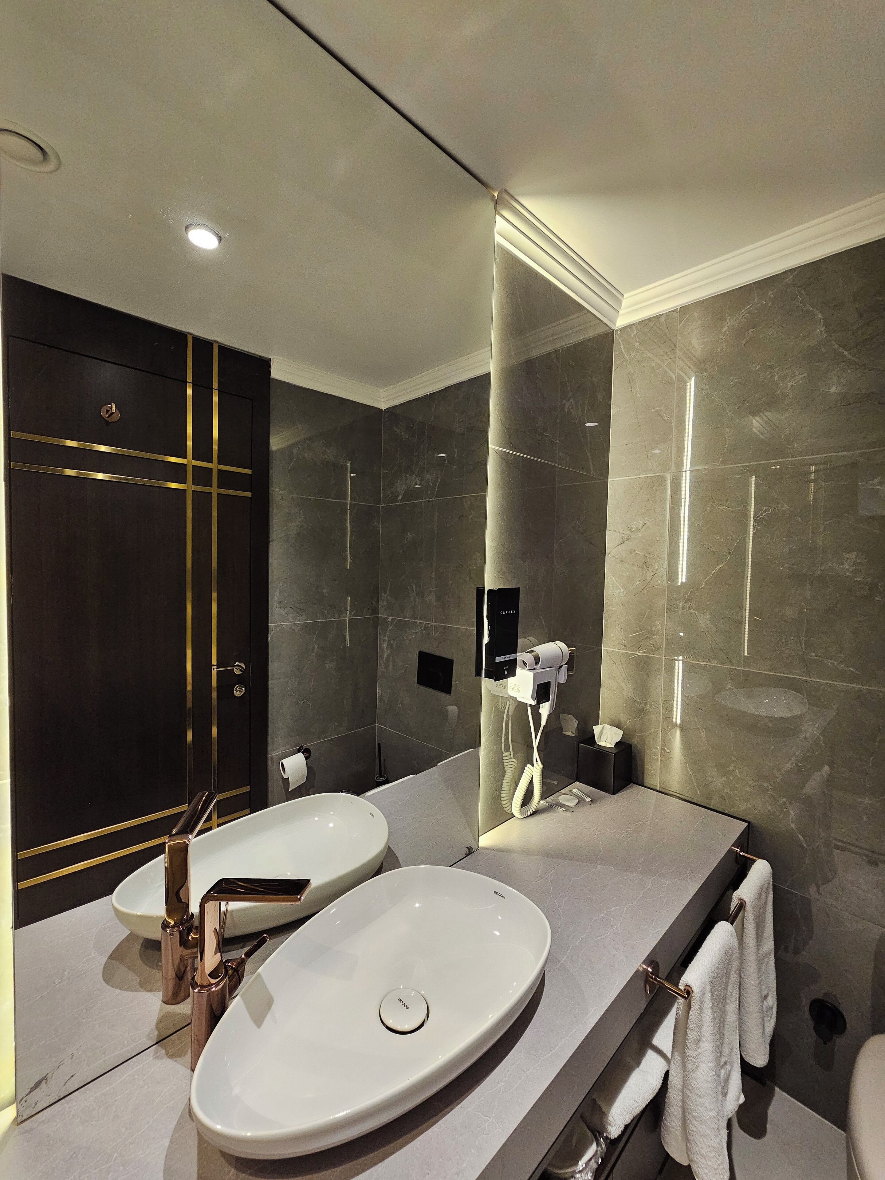 Une salle de bain moderne avec deux lavabos, un grand miroir et une porte en bois foncé.