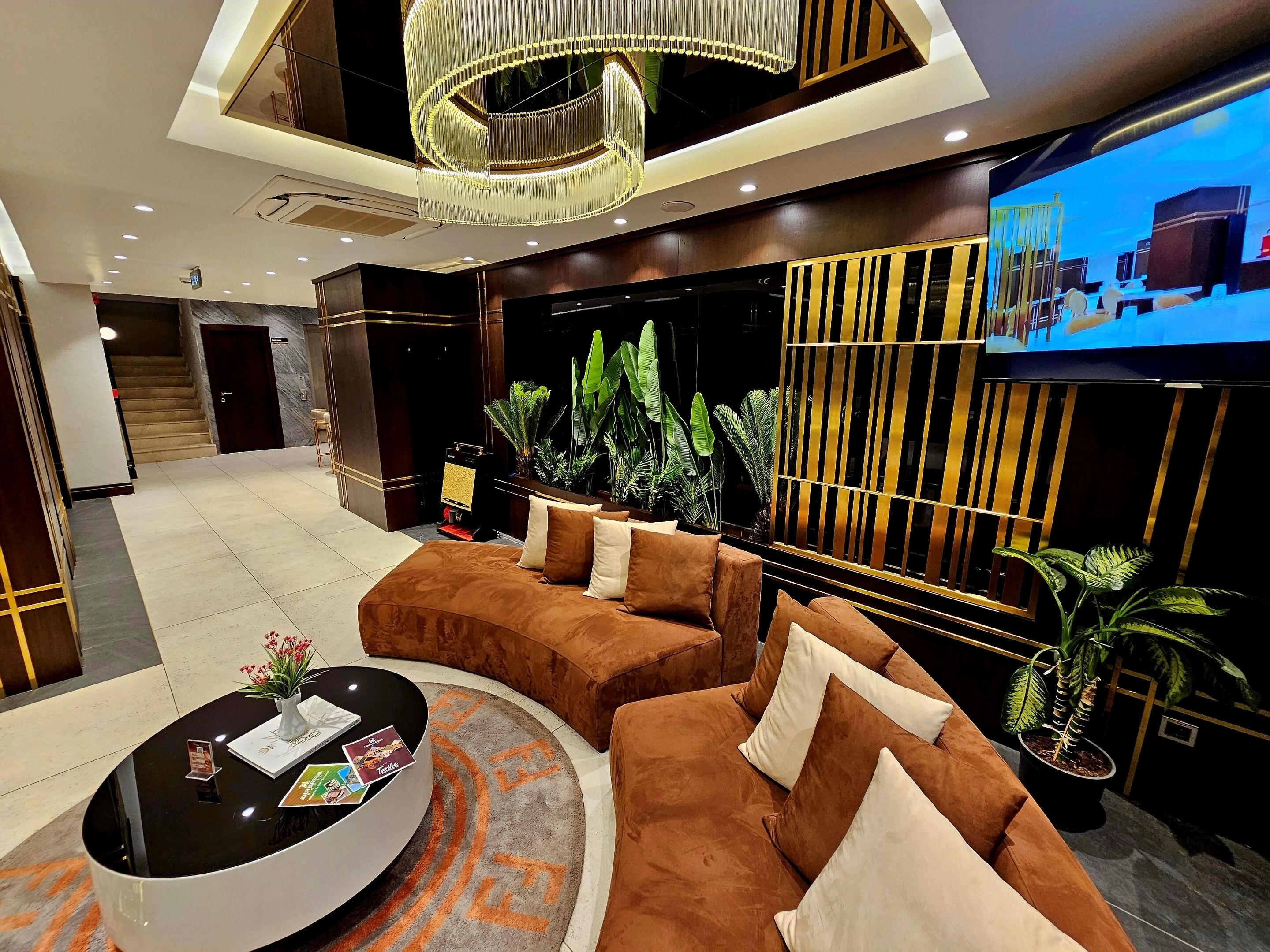 A modern lobby with a curved brown sofa, a round black coffee table, and a TV mounted on the wall.