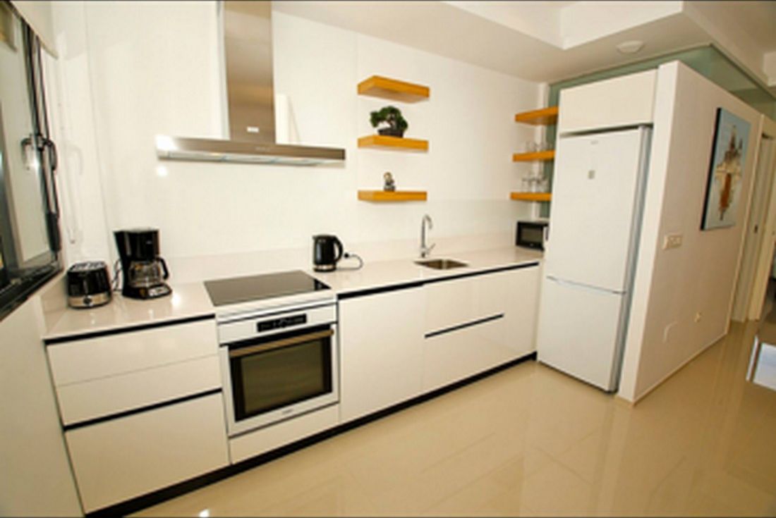 A modern kitchen with white cabinetry, a built-in oven, a coffee maker, and a refrigerator.