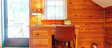 Una habitación de madera con escritorio, silla y ventana con cortinas.