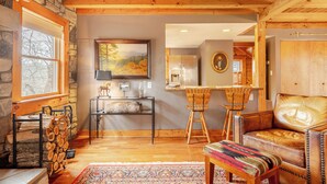 Ein gemütliches Interieur mit Steinwand, Holzbalkendecke, Kamin, Essbereich und einer Ledersofa.