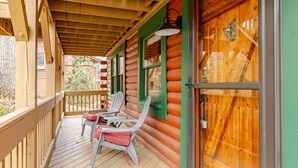 Eine Holzhütte mit Veranda, zwei Adirondack-Stühlen und einem kleinen Tisch.