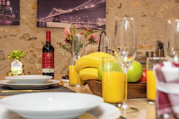 Uma mesa de jantar posta com pratos, uma garrafa de vinho, um vaso com flores e uma cesta de frutas.