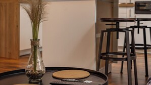 A modern kitchen with a wooden bar counter, a glass vase with dried plants, and a remote control on a round coaster. - Le Loft - Rated 5 Stars (Mussidan)