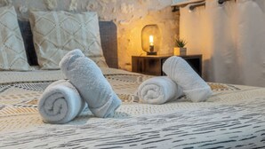 A neatly made bed with rolled towels, a bedside lamp, and a small table with a plant. - Le Loft - Rated 5 Stars (Mussidan)