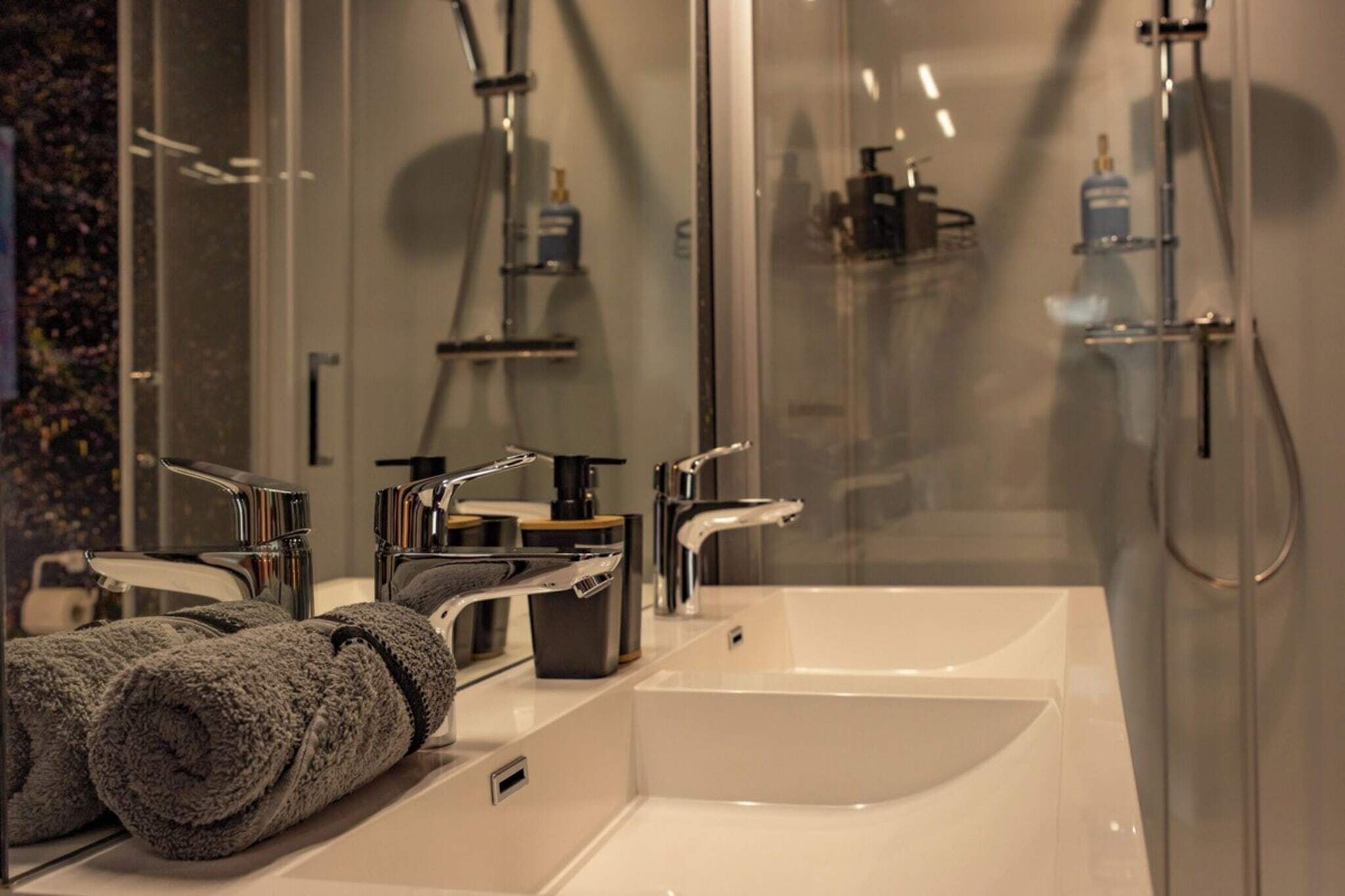 Een moderne badkamer met een douchecabine van glas, dubbele wastafels en een handdoekrek.