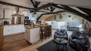 A modern kitchen with a central island, wooden beams, and a stone wall in the background. - Le Loft - Rated 5 Stars (Mussidan)