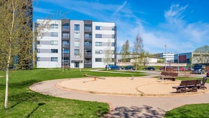 A modern apartment building with a landscaped park area, including a circular walking path and benches. - HARAKA APARTMENT WITH SUNSET BALCONY  (Tartu)