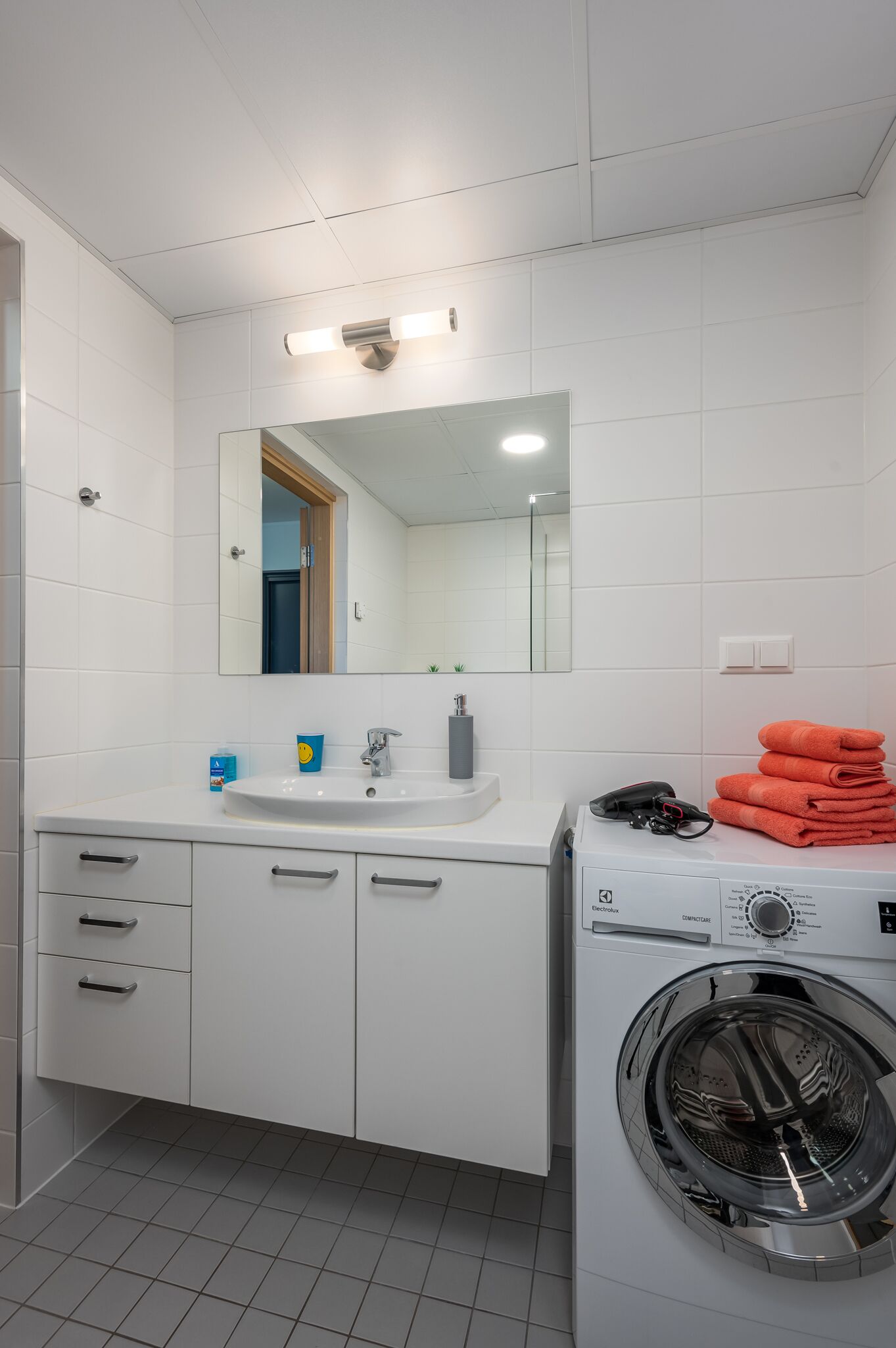 Une salle de bain moderne avec un lavabo blanc, un miroir et un lave-linge encastré.