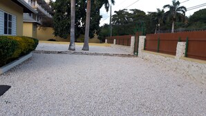Un barrio residencial con camino de grava, un edificio amarillo con contraventanas blancas y una cerca marrón.