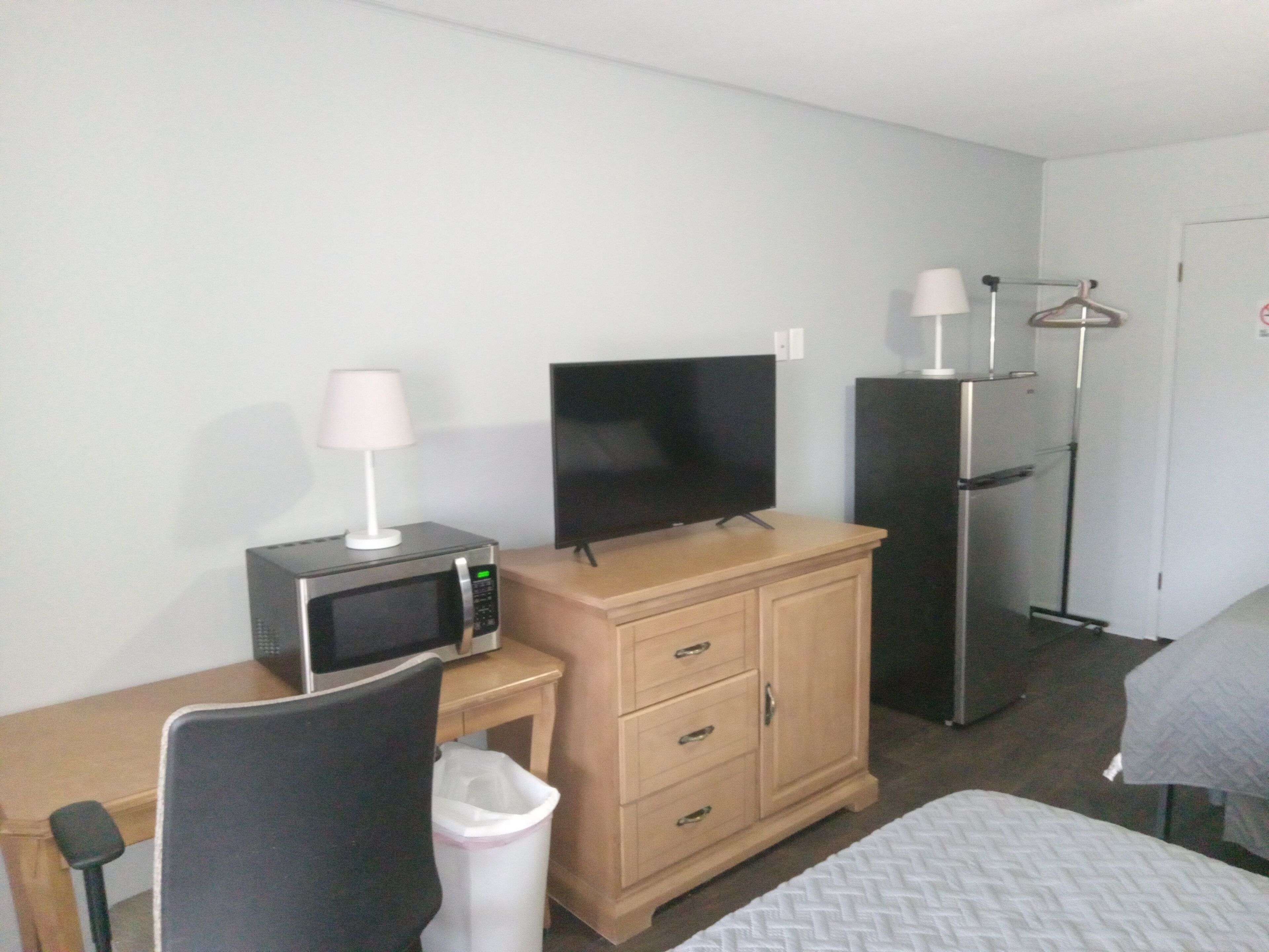 Habitación de hotel con cama, televisión, microondas, mesita, silla, armario y cubo de basura.