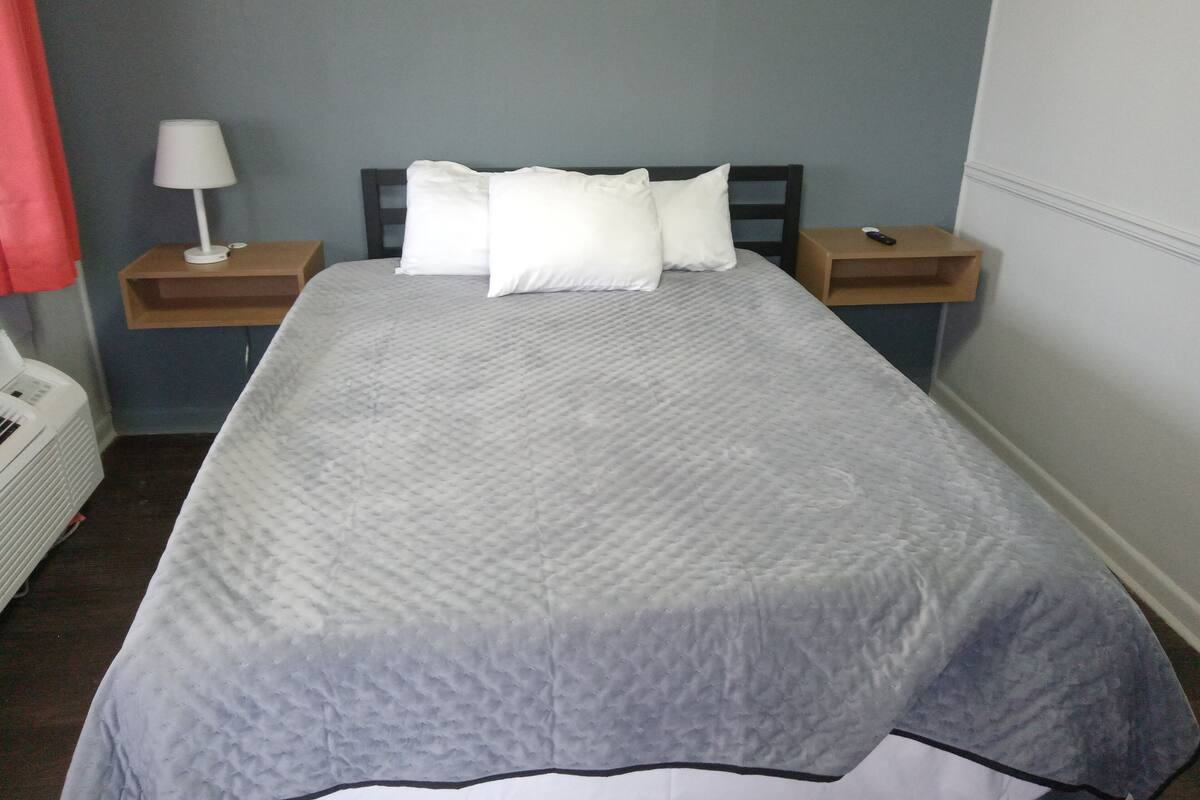 A neatly made bed with a grey quilt, two bedside tables with lamps, and a white heater on the floor.