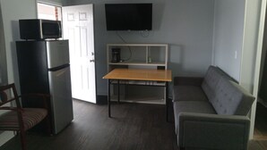 A compact living space with a kitchenette, a flat-screen TV mounted on the wall, a sofa, a dining table, and a chair. - Western Hills Motel (Versailles)