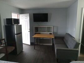 Un espacio habitable compacto con kitchenette, un televisor de pantalla plana montado en la pared, un sofá, una mesa de comedor y una silla.