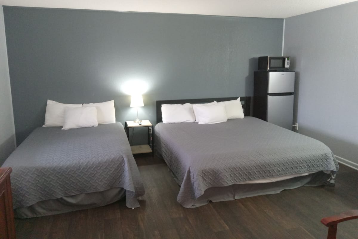 A room with two beds, a nightstand with a lamp, a microwave, and a refrigerator.