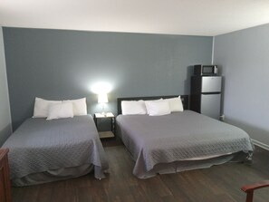A room with two beds, a nightstand with a lamp, a microwave, and a refrigerator. - Western Hills Motel (Versailles)