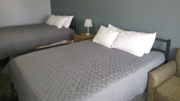A hotel room with two single beds, a nightstand with a lamp, and a chair. - Western Hills Motel (Versailles)