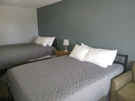 Una habitación de hotel con dos camas individuales, una mesita de noche con lámpara y una silla.