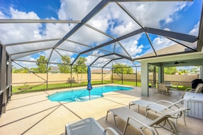 Uma área externa coberta com piscina, espreguiçadeiras e mesa de pátio.