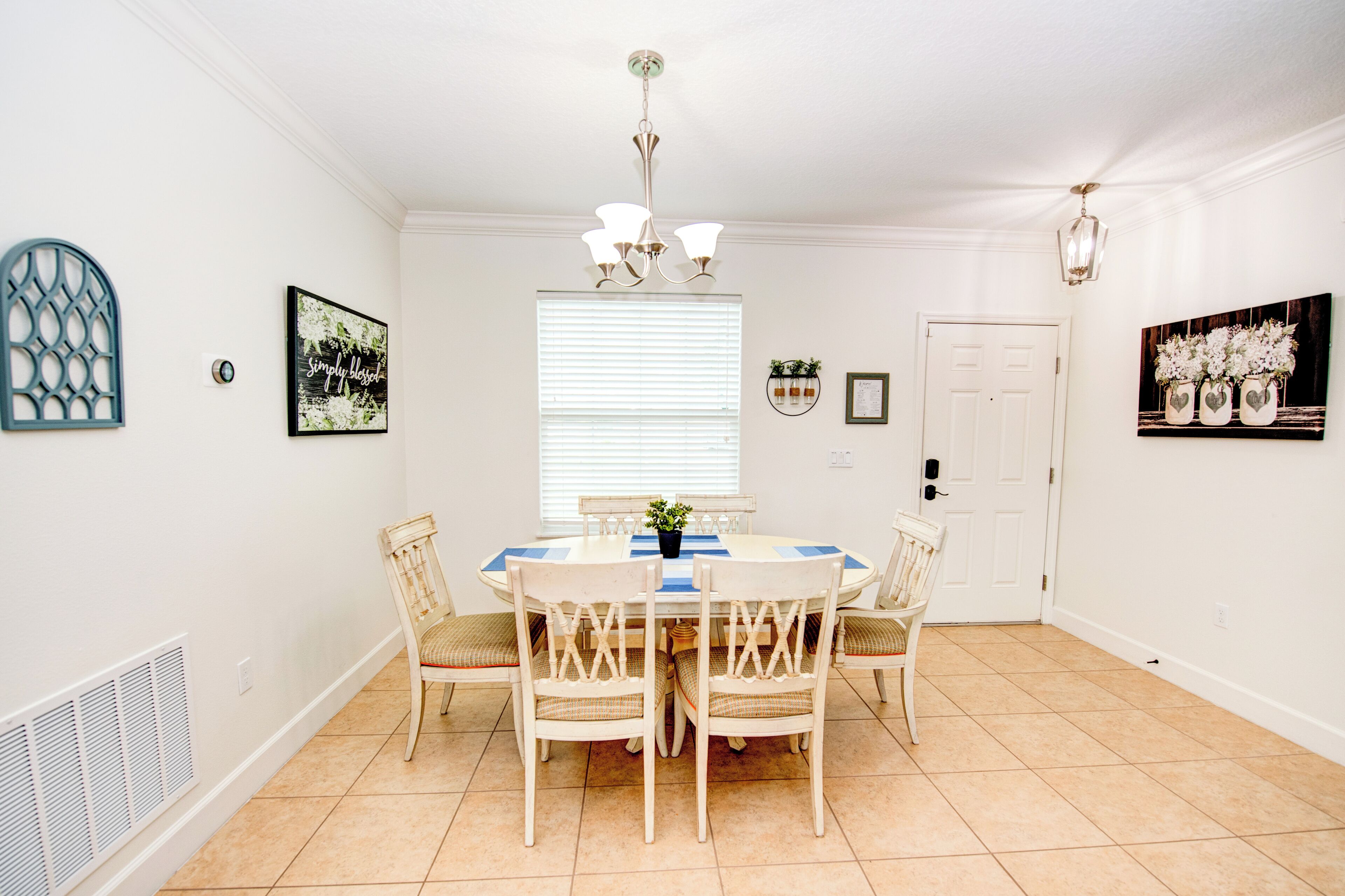 A dining room with a white table, four chairs, a chandelier, and wall art.