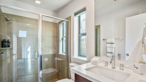 A modern bathroom with a glass-enclosed shower, a white sink with a mirror, and a toilet.