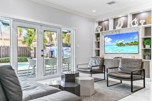 A modern living room with a TV, comfortable seating, and a view of a pool and outdoor area.