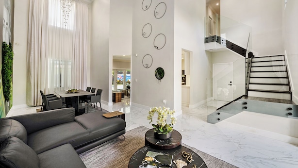 A modern living room with a grey sofa, a dining area, and a staircase. - Tropical Miami 5BR Retreat • Game Room • Pool_BBQ (Miami)