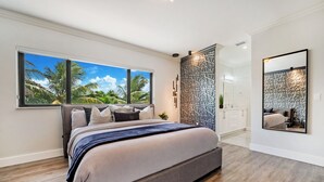 A modern bedroom with a large bed, a view of palm trees, and a decorative wall panel. - Tropical Miami 5BR Retreat • Game Room • Pool_BBQ (Miami)