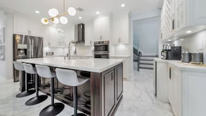 A modern kitchen with white cabinets, a marble countertop, and a central island with bar stools. - Tropical Miami 5BR Retreat • Game Room • Pool_BBQ (Miami)