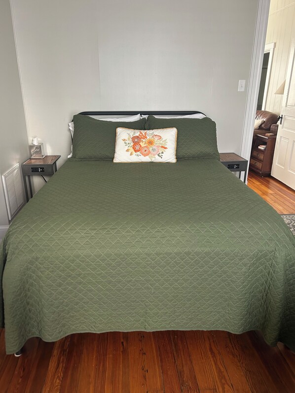 Una cama bien hecha con un edredón verde, una almohada floral y dos mesitas de noche con lámparas.